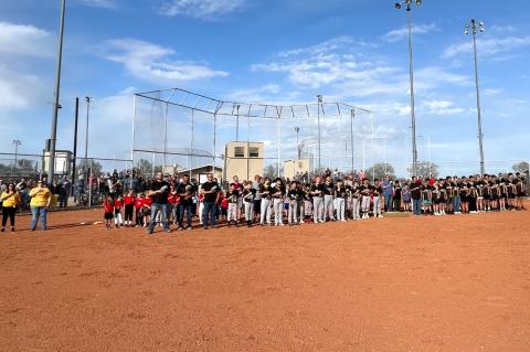 Over a hundred baseball players and their coaches turn to salute the flag as it is raised by members of the Buffalo Wallow Chapter of the Young Marines.