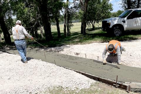 City employees Filiberto Herrera and Luis Vigil (in orange vest) prepared a drainage gutter on Lamar Street last week, in preparation for a road improvement project that will result in the first-time paving of six blocks of streets.