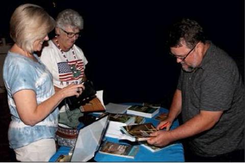 Stew Magnuson signed copies of several of his books after his presentation on Highway 83 at the Palace Theatre last Thursday. Queuing up for books were (left to right) Ginger Webb and Eline Burch. —photo by Cathy Ricketts