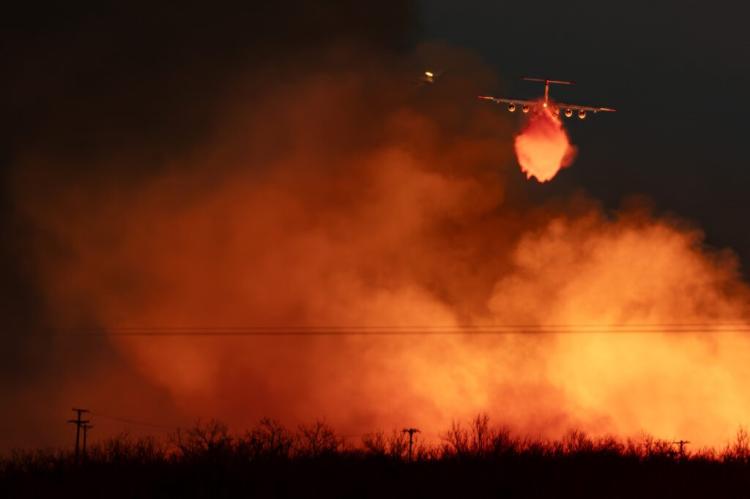 A Texas A&M Forest Service plane drops water on a wall of flames that reaches into the sky as the Smokehouse Creek fire reignited on March 3 near Miami. (Texas A&M AgriLife photo by Sam Craft)