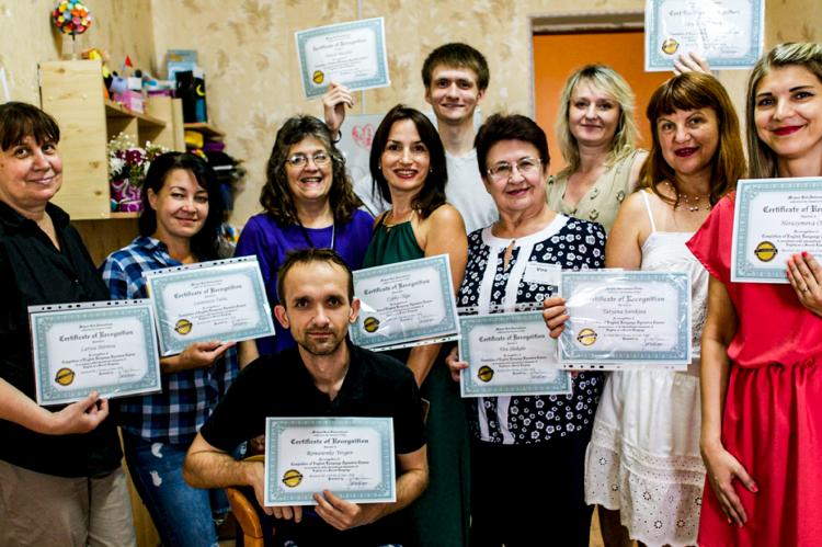 Bynum stands with a group of adult students proudly displaying their course completions diplomas. The class met in Azovstal, where a steel plant was targeted and destroyed by Russian bombs, along with many Ukrainian fighters who made their last stand there. The student in front was a worker at the plant. His fate is uncertain today, Bynum said.