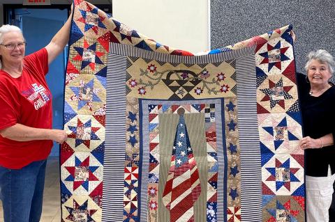 Freda Collier and Ilene Floyd display a quilt made for a veteran