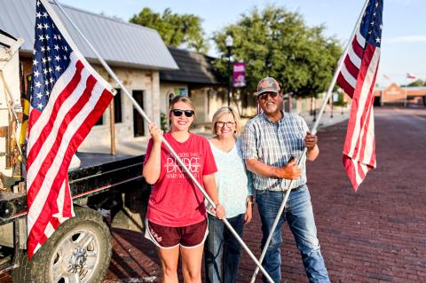 Steve and Linda Rader, and their daughter, Sarah Rader, worked as a team Tuesday, placing flags in front of downtown businesses. PHOTO BY ANNA BOOZE